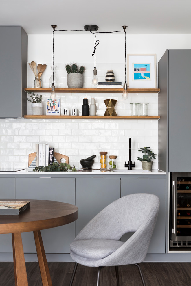 Mid-sized contemporary single-wall eat-in kitchen in London with flat-panel cabinets, grey cabinets, white splashback, subway tile splashback, dark hardwood floors, brown floor, white benchtop and an undermount sink.