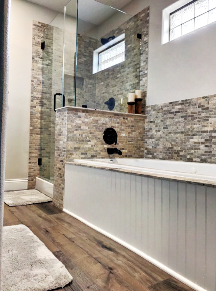 Mid-sized country master bathroom in Houston with white cabinets, a drop-in tub, an open shower, travertine, grey walls, laminate floors, a drop-in sink, granite benchtops, brown floor, a hinged shower door and black benchtops.