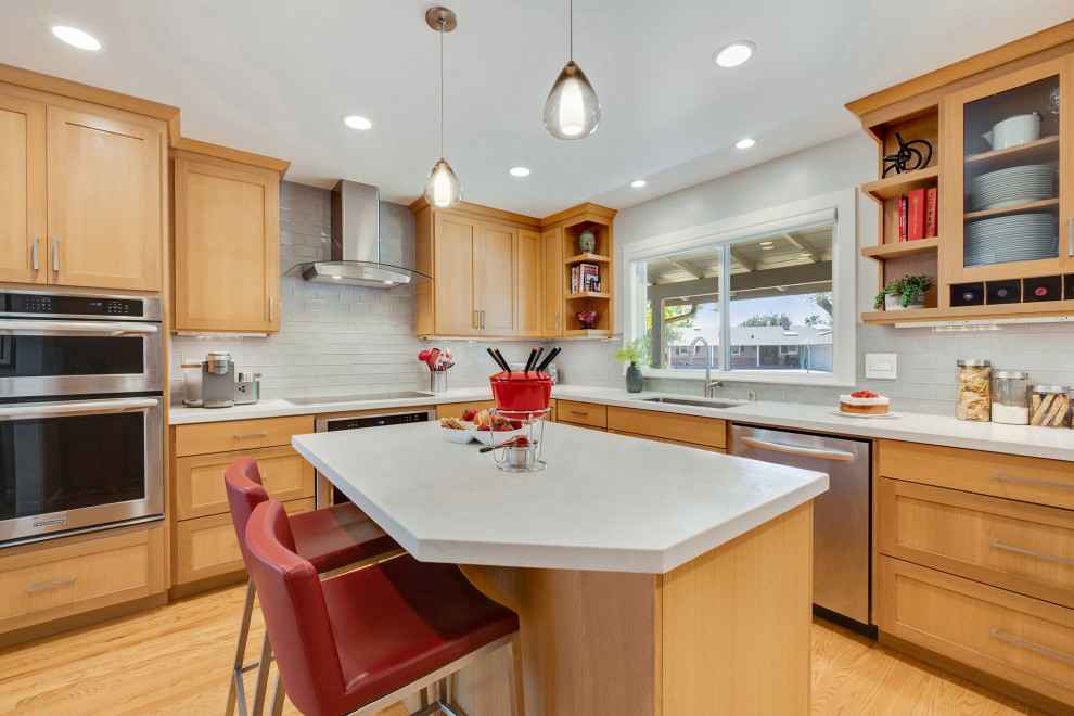 This is an example of a transitional l-shaped eat-in kitchen in San Francisco with an undermount sink, shaker cabinets, medium wood cabinets, grey splashback, glass tile splashback, stainless steel appliances, medium hardwood floors, with island, brown floor and white benchtop.
