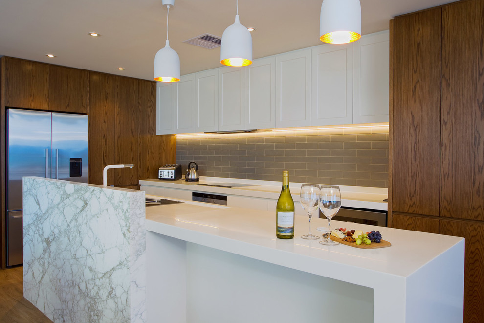 This is an example of a mid-sized beach style galley open plan kitchen in Gold Coast - Tweed with an undermount sink, quartz benchtops, grey splashback, subway tile splashback, stainless steel appliances, vinyl floors, with island, flat-panel cabinets and medium wood cabinets.