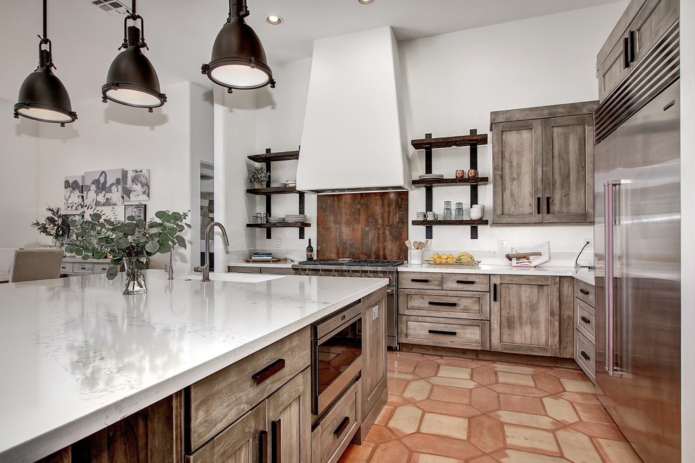 Mid-sized industrial l-shaped eat-in kitchen in Phoenix with an undermount sink, shaker cabinets, distressed cabinets, quartz benchtops, brown splashback, porcelain splashback, stainless steel appliances, terra-cotta floors, with island and white benchtop.
