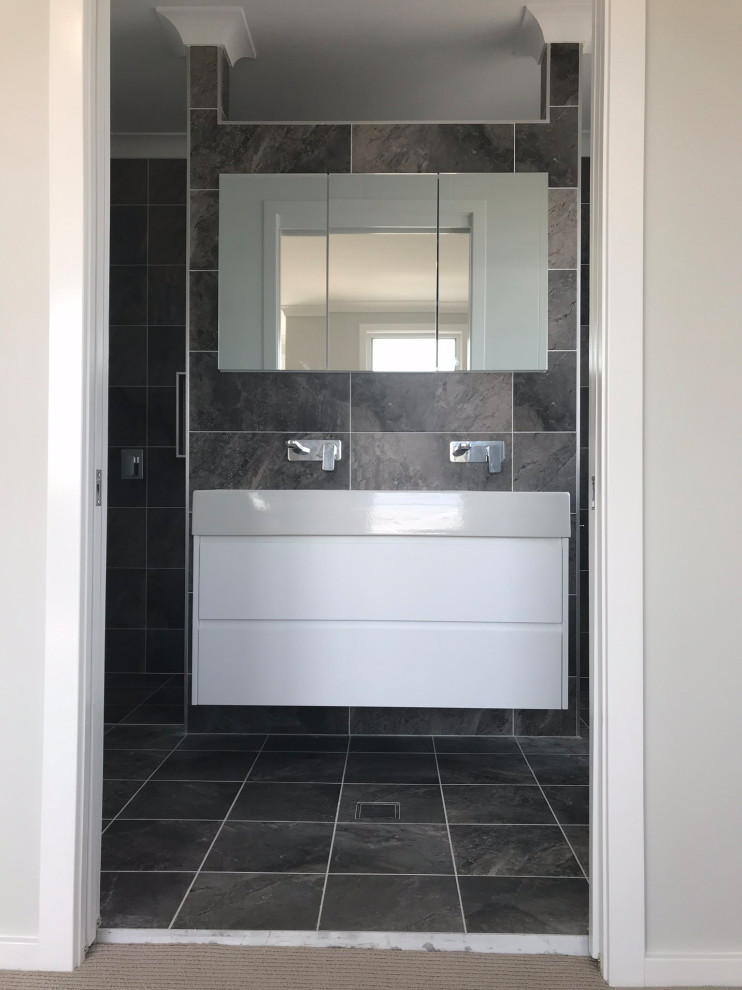 This is an example of a large beach style master bathroom in Central Coast with furniture-like cabinets, white cabinets, a freestanding tub, a double shower, a one-piece toilet, gray tile, porcelain tile, grey walls, porcelain floors, a trough sink, solid surface benchtops, grey floor and white benchtops.