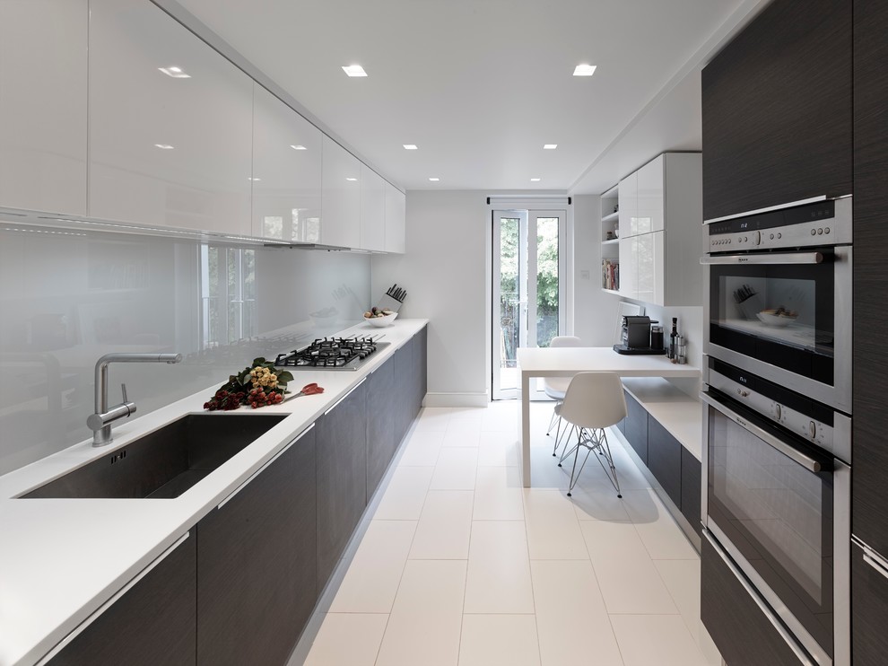 Photo of a medium sized contemporary galley open plan kitchen in London with an integrated sink, flat-panel cabinets, dark wood cabinets, engineered stone countertops, grey splashback, glass sheet splashback, stainless steel appliances, travertine flooring and no island.
