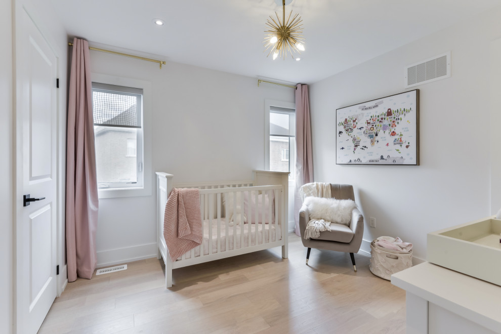 Photo of a contemporary nursery for girls in Toronto with white walls and light hardwood floors.