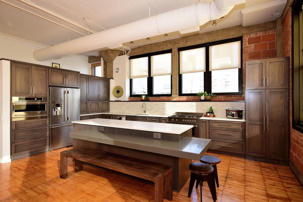 Inspiration for a large industrial u-shaped eat-in kitchen in Chicago with dark wood cabinets, white splashback, stainless steel appliances, medium hardwood floors, with island, a drop-in sink, recessed-panel cabinets, granite benchtops, terra-cotta splashback and brown floor.