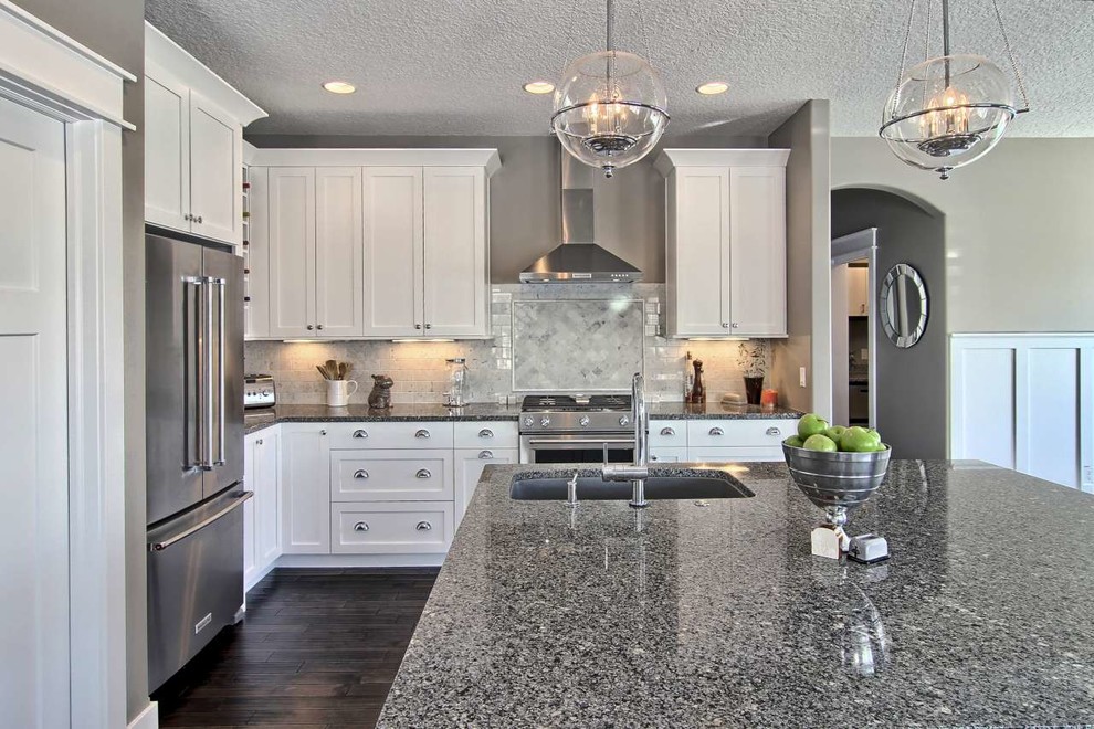 Open concept kitchen - mid-sized transitional l-shaped dark wood floor open concept kitchen idea with a single-bowl sink, shaker cabinets, white cabinets, granite countertops, gray backsplash, stone tile backsplash, stainless steel appliances and an island