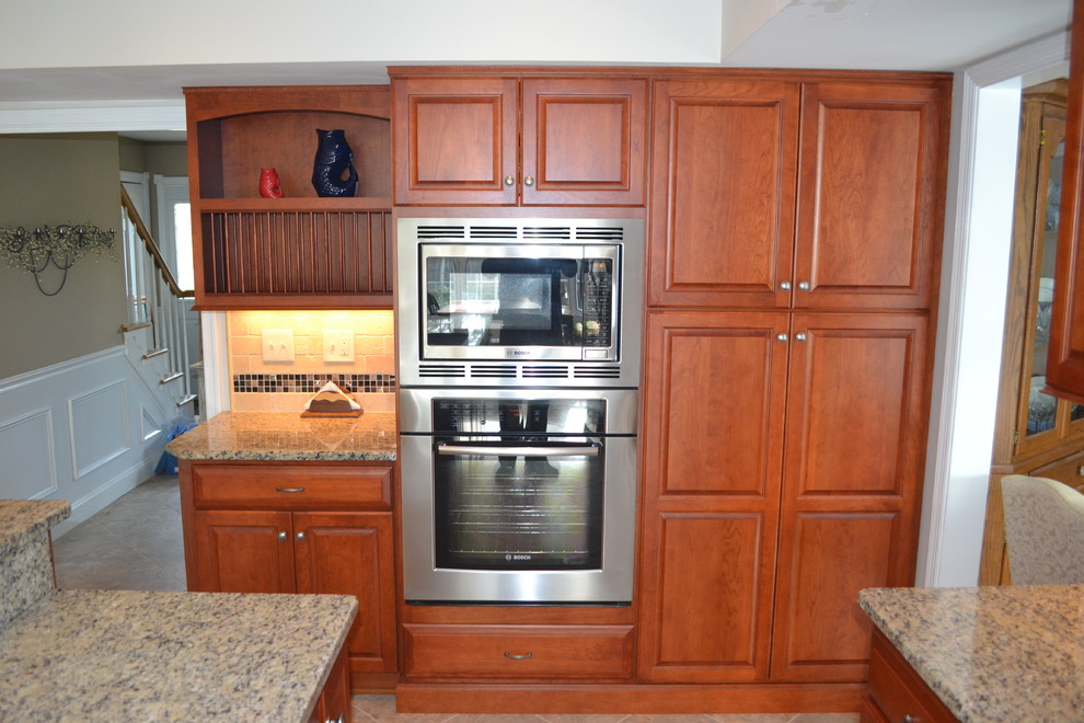 Photo of a transitional u-shaped eat-in kitchen in Philadelphia with an undermount sink, raised-panel cabinets, medium wood cabinets, granite benchtops, beige splashback, ceramic splashback and stainless steel appliances.