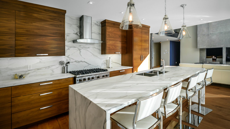 This is an example of a mid-sized midcentury l-shaped eat-in kitchen in Toronto with flat-panel cabinets, medium wood cabinets, marble benchtops, with island, an undermount sink, grey splashback, panelled appliances and medium hardwood floors.