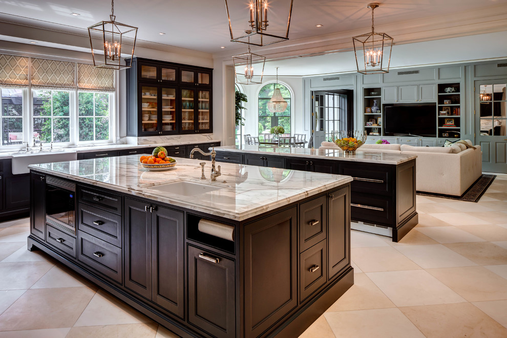 Transitional open plan kitchen in Houston with a farmhouse sink, recessed-panel cabinets, black cabinets, marble benchtops, grey splashback, marble splashback, stainless steel appliances, multiple islands, beige floor and grey benchtop.