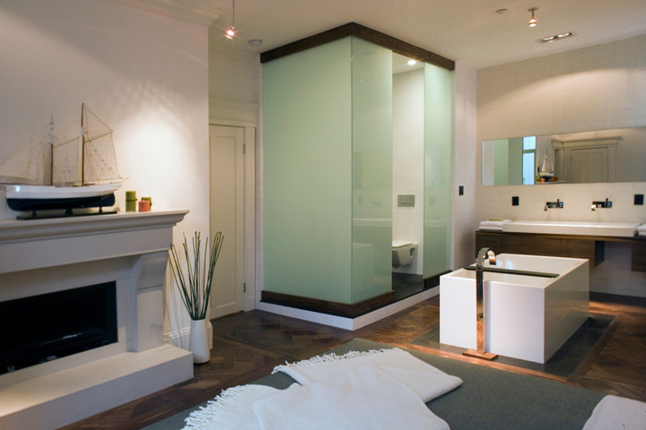Inspiration for a mid-sized contemporary master bathroom in San Francisco with a wall-mount sink, a freestanding tub, a wall-mount toilet, medium wood cabinets, white tile, flat-panel cabinets, solid surface benchtops, a corner shower, porcelain tile, white walls and medium hardwood floors.
