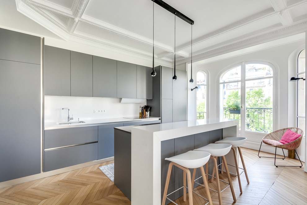 Photo of a large contemporary single-wall eat-in kitchen in Paris with an undermount sink, flat-panel cabinets, grey cabinets, white splashback, light hardwood floors, with island and panelled appliances.