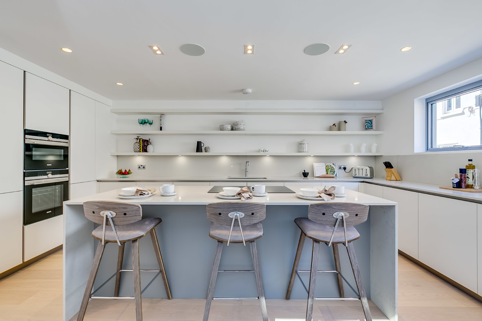 This is an example of a large contemporary u-shaped eat-in kitchen in London with flat-panel cabinets, marble benchtops, white benchtop, an undermount sink, white cabinets, white splashback, light hardwood floors, with island and beige floor.