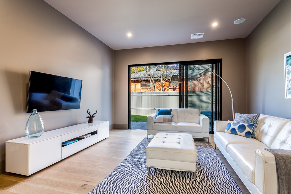 This is an example of a contemporary enclosed living room in Adelaide with brown walls, light hardwood floors, a wall-mounted tv and beige floor.