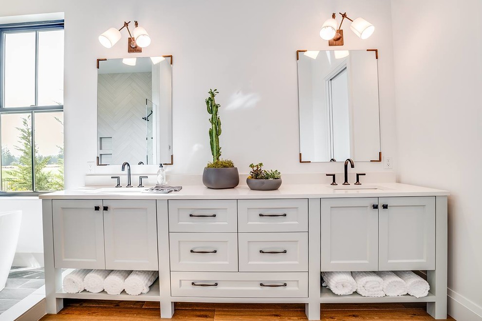 Inspiration for a large country master bathroom in Portland with a freestanding tub, recessed-panel cabinets, white cabinets, beige tile, medium hardwood floors, an undermount sink and white benchtops.