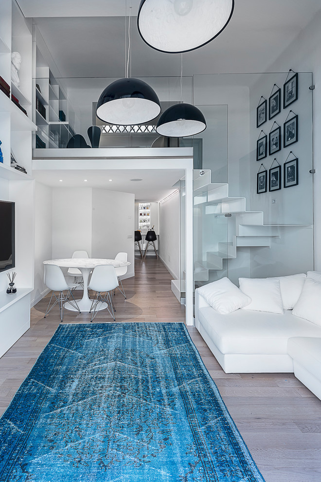 Photo of a mid-sized contemporary loft-style family room in Milan with white walls, medium hardwood floors, no fireplace and a wall-mounted tv.