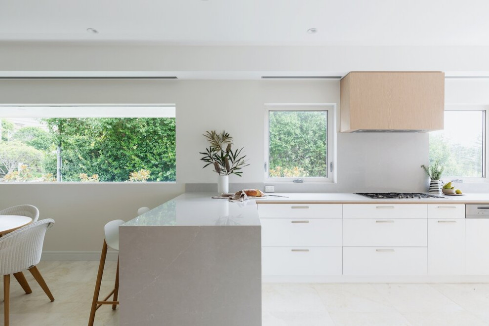 Photo of a mid-sized beach style l-shaped eat-in kitchen in Sydney with white cabinets, marble benchtops, grey splashback, marble splashback, ceramic floors, beige floor, grey benchtop, flat-panel cabinets and a peninsula.