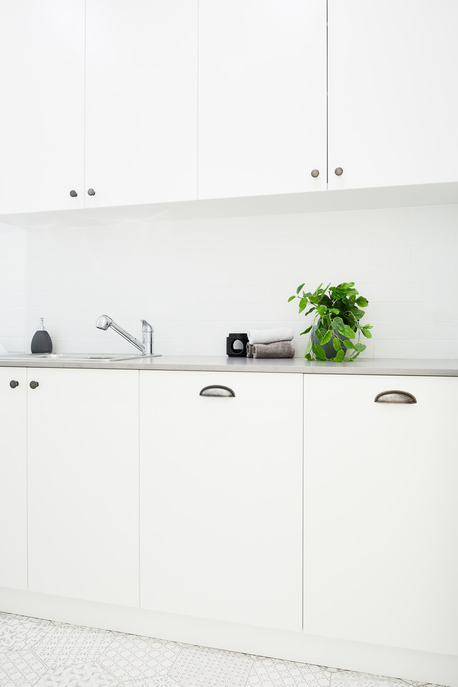 Photo of a mid-sized beach style single-wall utility room in Sydney with a double-bowl sink, flat-panel cabinets, white cabinets, quartz benchtops, white walls, ceramic floors and grey benchtop.