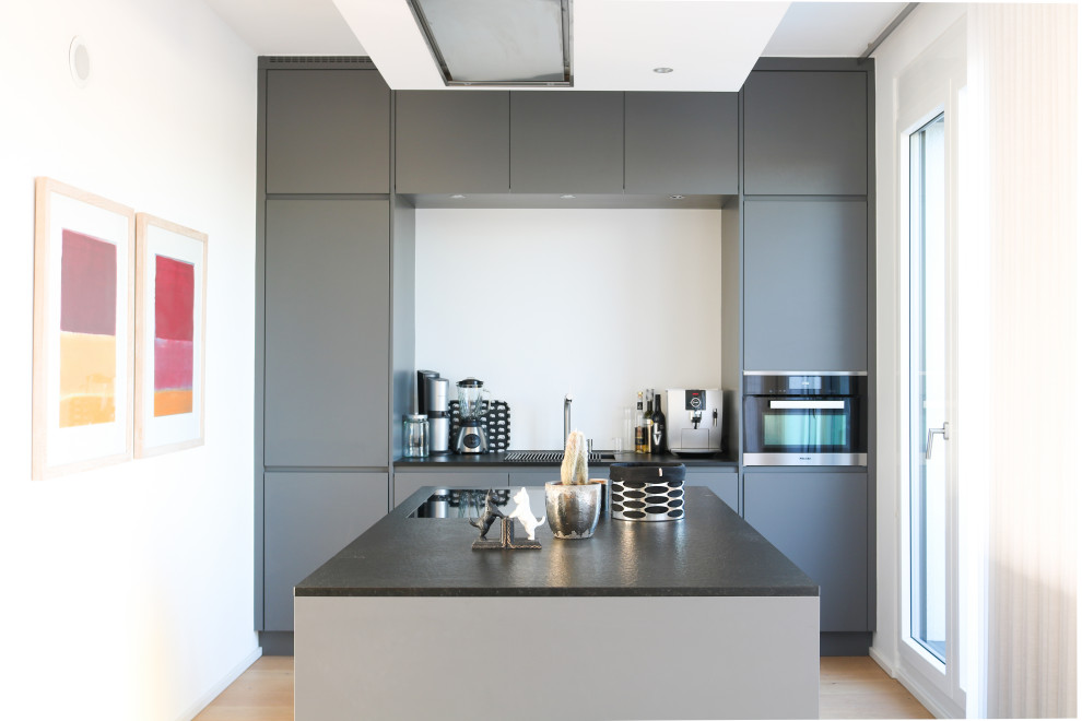 Offene Moderne Küche in grau-weiß mit grauen Schränken, Granit-Arbeitsplatte, Küchenrückwand in Weiß, Kücheninsel und schwarzer Arbeitsplatte