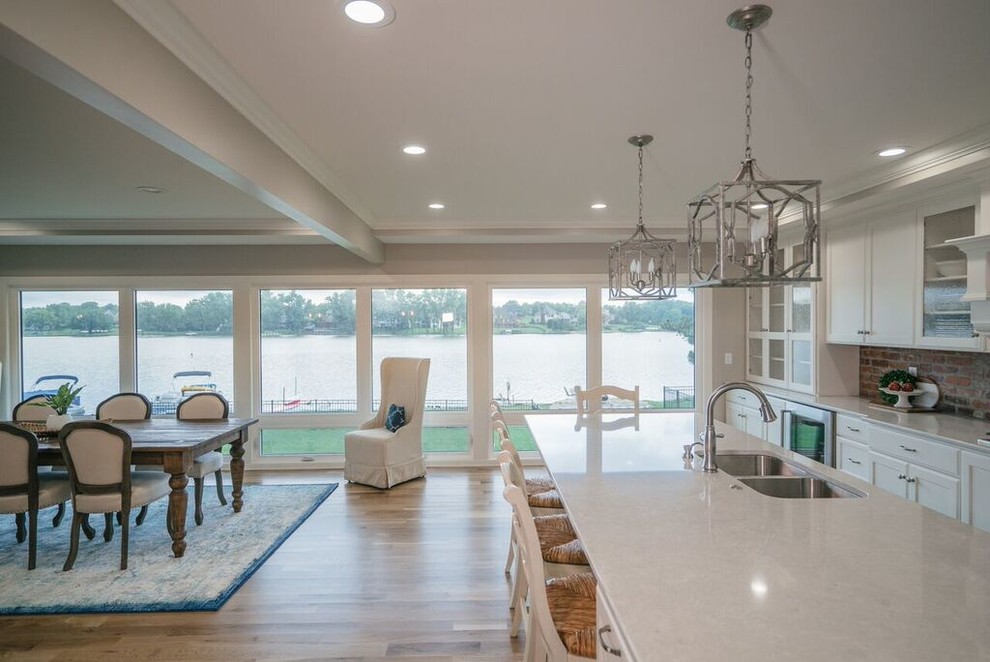 Huge l-shaped light wood floor and brown floor open concept kitchen photo with a double-bowl sink, recessed-panel cabinets, brick backsplash, stainless steel appliances and an island