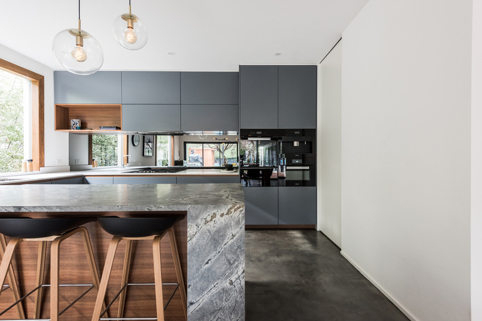 Inspiration for a large contemporary u-shaped eat-in kitchen in Melbourne with an undermount sink, flat-panel cabinets, blue cabinets, granite benchtops, metallic splashback, mirror splashback, black appliances, concrete floors, a peninsula, grey floor and grey benchtop.