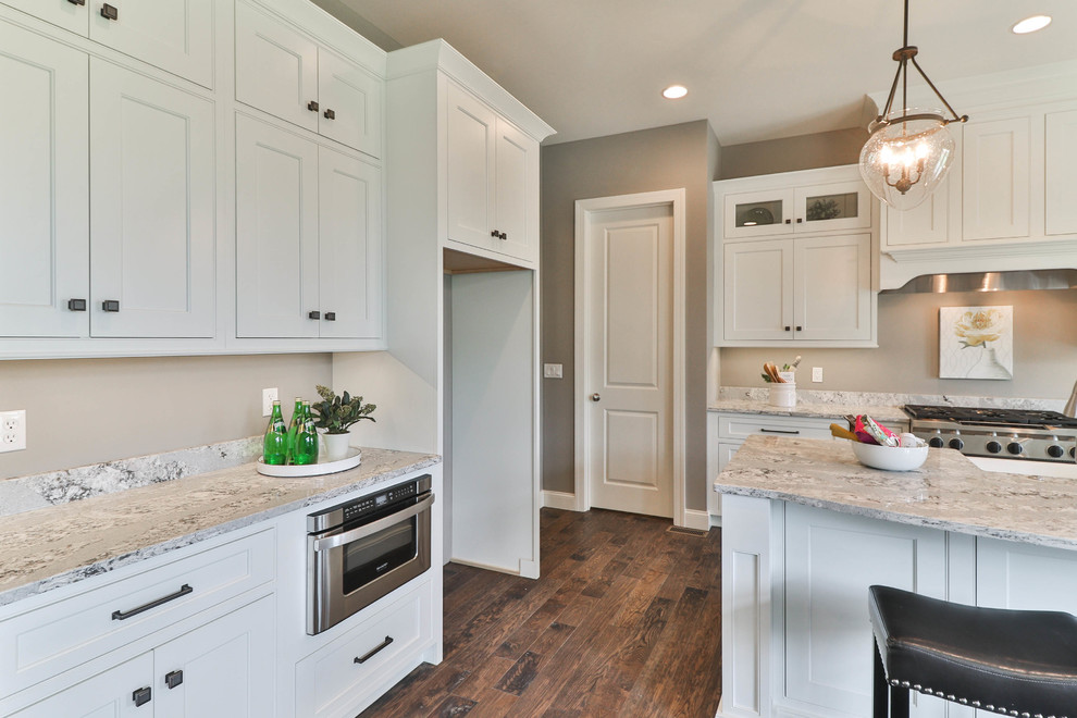 Open concept kitchen - mid-sized transitional l-shaped dark wood floor and brown floor open concept kitchen idea in St Louis with a farmhouse sink, shaker cabinets, white cabinets, granite countertops, gray backsplash, stainless steel appliances and an island