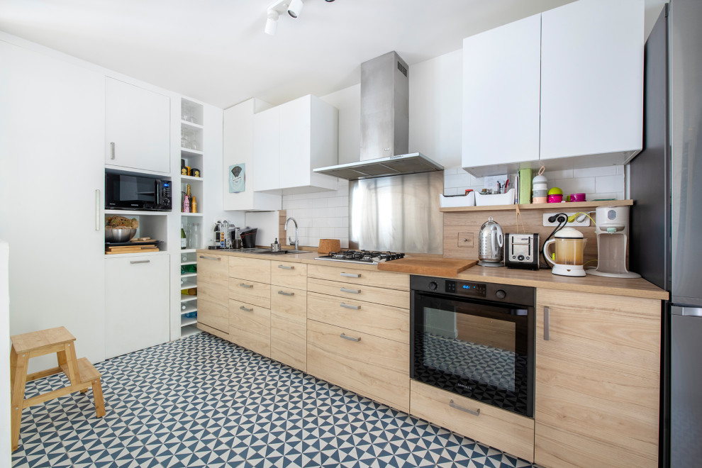 パリにあるお手頃価格の中くらいな北欧スタイルのおしゃれなキッチン (ドロップインシンク、フラットパネル扉のキャビネット、淡色木目調キャビネット、木材カウンター、ベージュキッチンパネル、木材のキッチンパネル、シルバーの調理設備、セメントタイルの床、アイランドなし、青い床、ベージュのキッチンカウンター) の写真