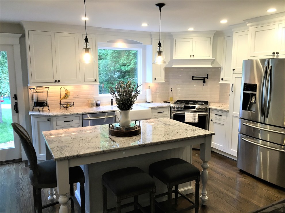 Photo of a mid-sized transitional l-shaped separate kitchen in New York with a farmhouse sink, shaker cabinets, white cabinets, marble benchtops, white splashback, subway tile splashback, stainless steel appliances, dark hardwood floors, with island and brown floor.