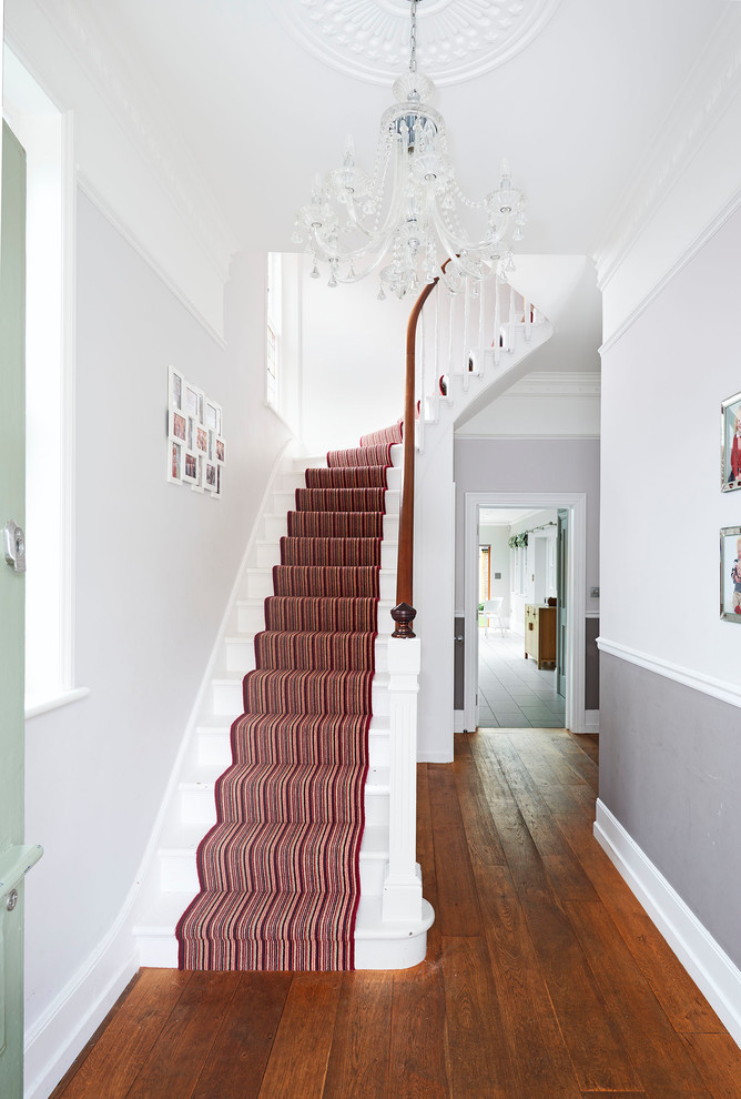 Transitional painted wood curved staircase in London with painted wood risers and wood railing.
