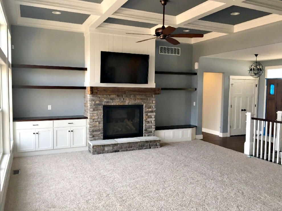 Photo of a mid-sized transitional open concept family room in Other with grey walls, carpet, a standard fireplace, a brick fireplace surround, a wall-mounted tv and beige floor.