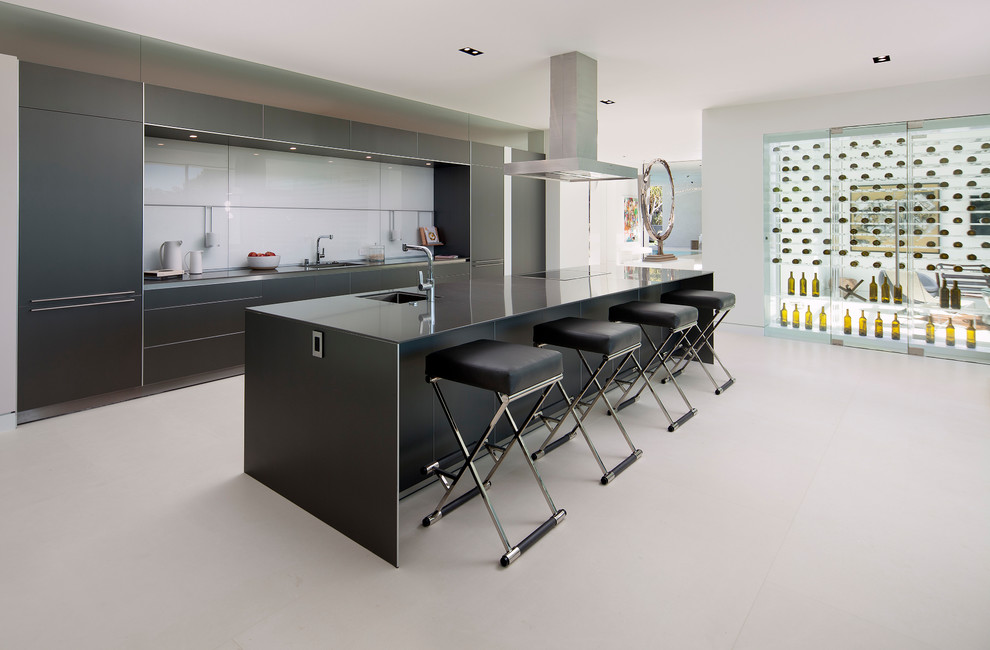 Large contemporary single-wall open plan kitchen in Los Angeles with an undermount sink, flat-panel cabinets, black cabinets, white splashback, glass sheet splashback, with island, white floor, solid surface benchtops, panelled appliances, concrete floors and black benchtop.