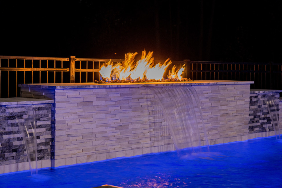 Diseño de piscina moderna grande rectangular en patio trasero con adoquines de piedra natural