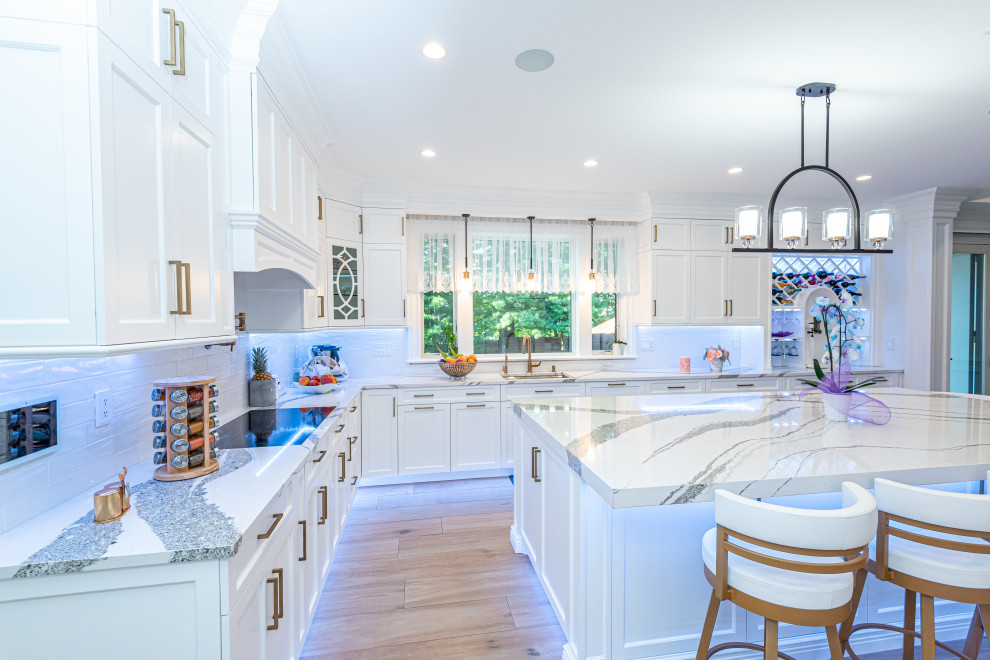 Transitional l-shaped kitchen in New York with an undermount sink, shaker cabinets, white cabinets, white splashback, panelled appliances, light hardwood floors, with island, beige floor and white benchtop.