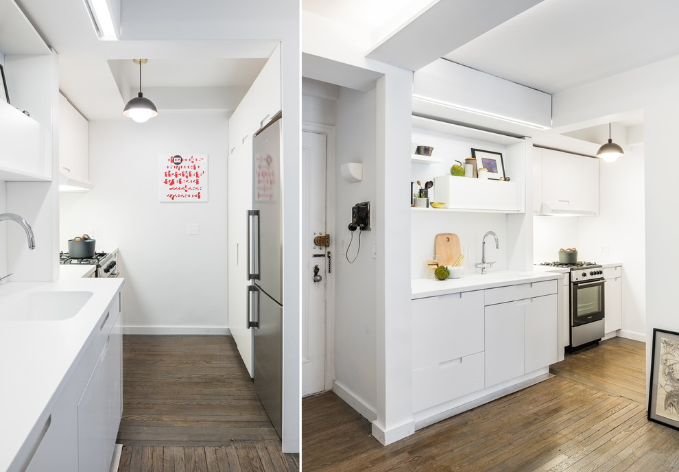 Photo of a small modern galley kitchen pantry in New York with an integrated sink, flat-panel cabinets, white cabinets, solid surface benchtops, white splashback, medium hardwood floors and no island.