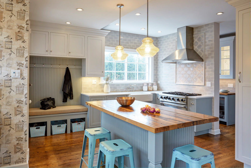 This is an example of a transitional kitchen in Chicago with a farmhouse sink, shaker cabinets, blue cabinets, subway tile splashback, stainless steel appliances, medium hardwood floors, with island, brown floor and brown benchtop.