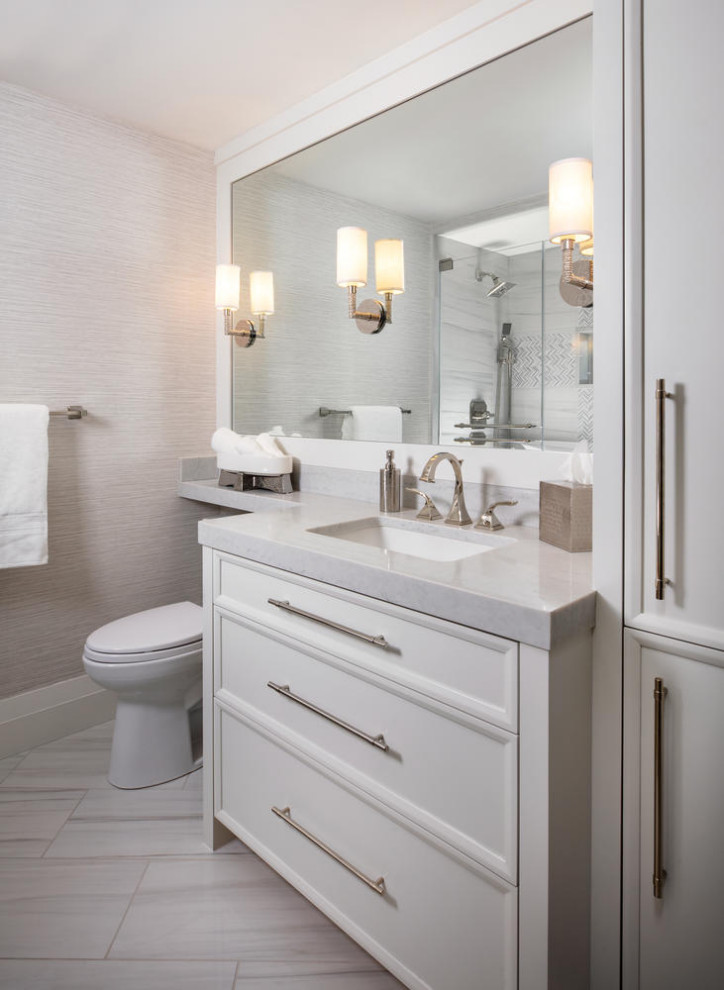 Design ideas for a mid-sized beach style 3/4 bathroom in Miami with recessed-panel cabinets, white cabinets, an alcove shower, a one-piece toilet, gray tile, porcelain tile, grey walls, porcelain floors, an integrated sink, engineered quartz benchtops, grey floor, a hinged shower door, grey benchtops, a single vanity, a built-in vanity and wallpaper.