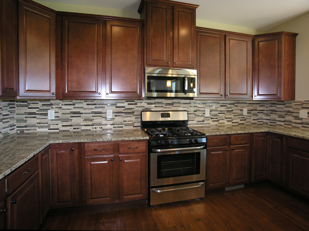 This is an example of a mid-sized traditional u-shaped kitchen in Chicago with raised-panel cabinets, dark wood cabinets, granite benchtops, brown splashback, ceramic splashback, stainless steel appliances, dark hardwood floors, no island and brown floor.