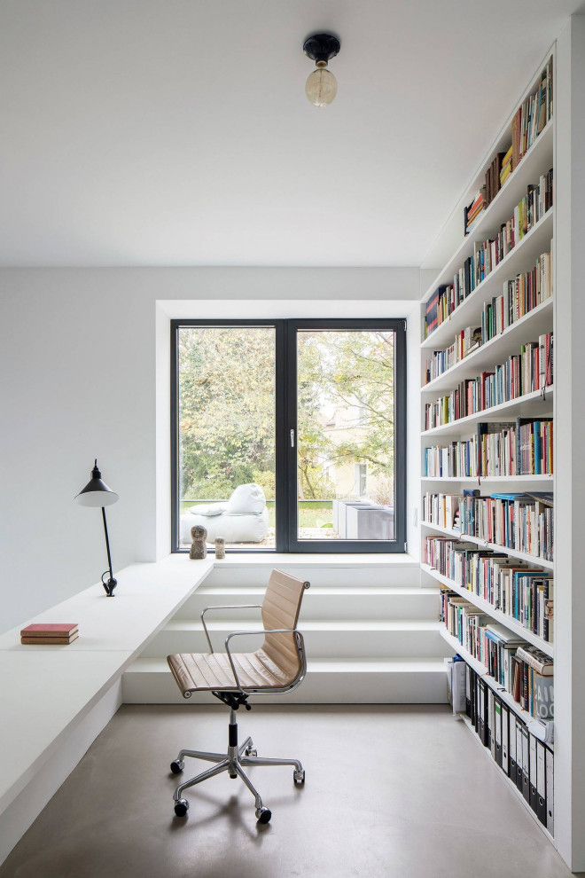 Bild på ett funkis hemmabibliotek, med vita väggar, ett inbyggt skrivbord och grått golv