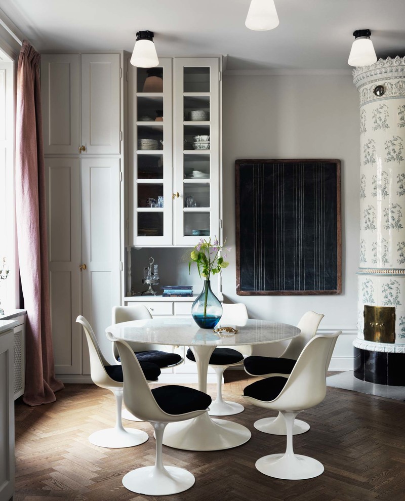Photo of a mid-sized eclectic kitchen/dining combo in Stockholm with white walls, medium hardwood floors and a corner fireplace.
