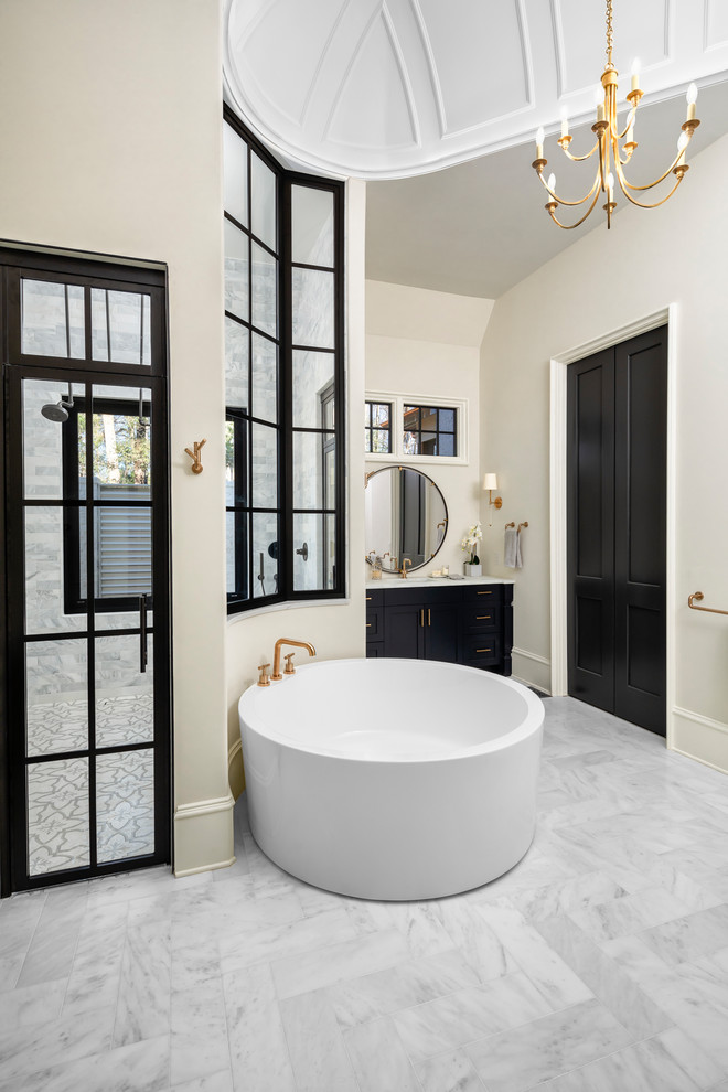 Photo of a large transitional master bathroom in Charlotte with a freestanding tub, a curbless shower, marble floors, a hinged shower door, shaker cabinets, black cabinets, beige walls, grey floor and white benchtops.