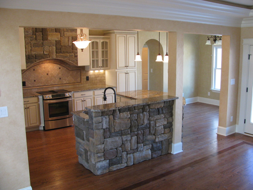 Example of a mid-sized transitional medium tone wood floor eat-in kitchen design with an undermount sink, raised-panel cabinets, yellow cabinets, granite countertops, yellow backsplash, stone tile backsplash, stainless steel appliances and an island