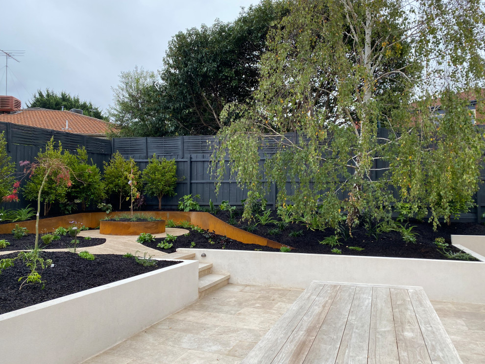 Стильный дизайн: маленький осенний участок и сад на заднем дворе с клумбами, полуденной тенью, покрытием из каменной брусчатки и с деревянным забором для на участке и в саду - последний тренд
