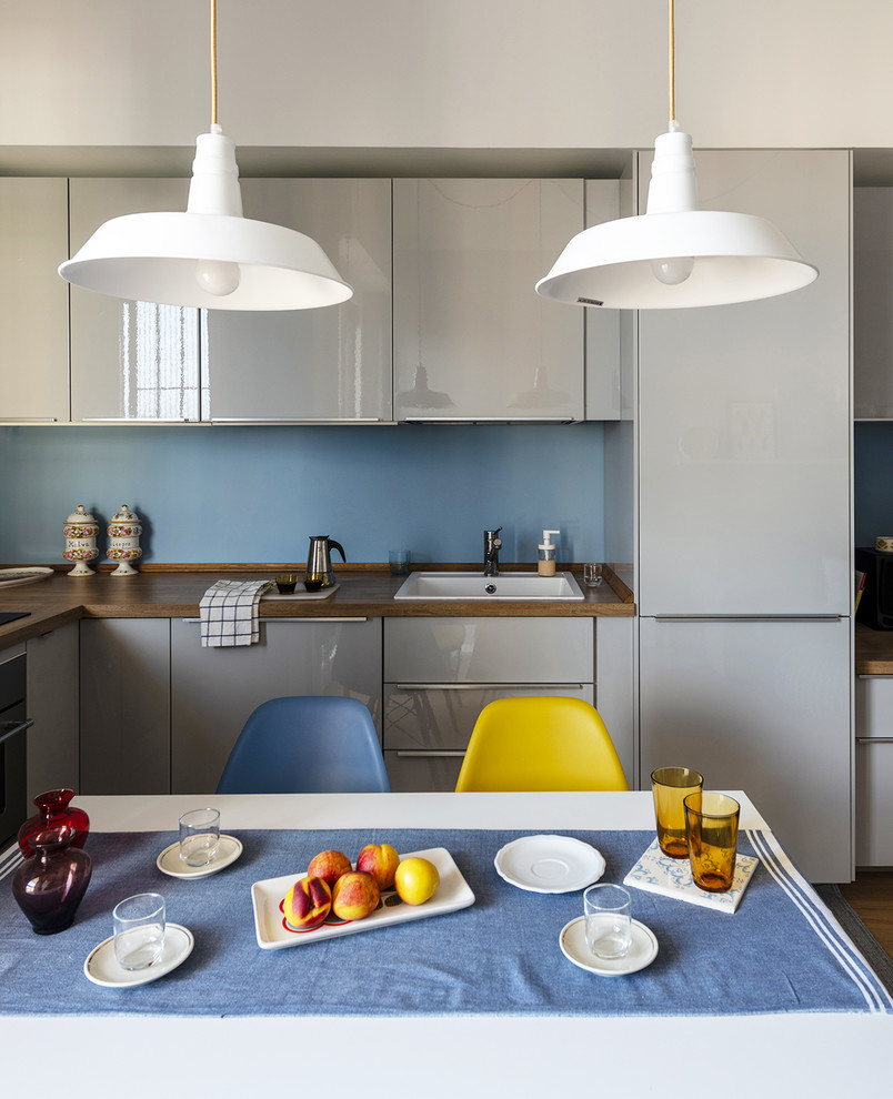 This is an example of a small contemporary l-shaped eat-in kitchen in Milan with a drop-in sink, flat-panel cabinets, grey cabinets, laminate benchtops, blue splashback, metal splashback, panelled appliances, light hardwood floors, no island, beige floor and brown benchtop.