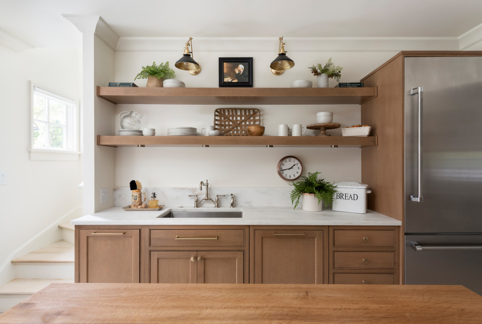Design ideas for a mid-sized traditional galley separate kitchen in Chicago with a drop-in sink, beaded inset cabinets, medium wood cabinets, marble benchtops, metallic splashback, mirror splashback, stainless steel appliances, light hardwood floors, with island, brown floor and white benchtop.