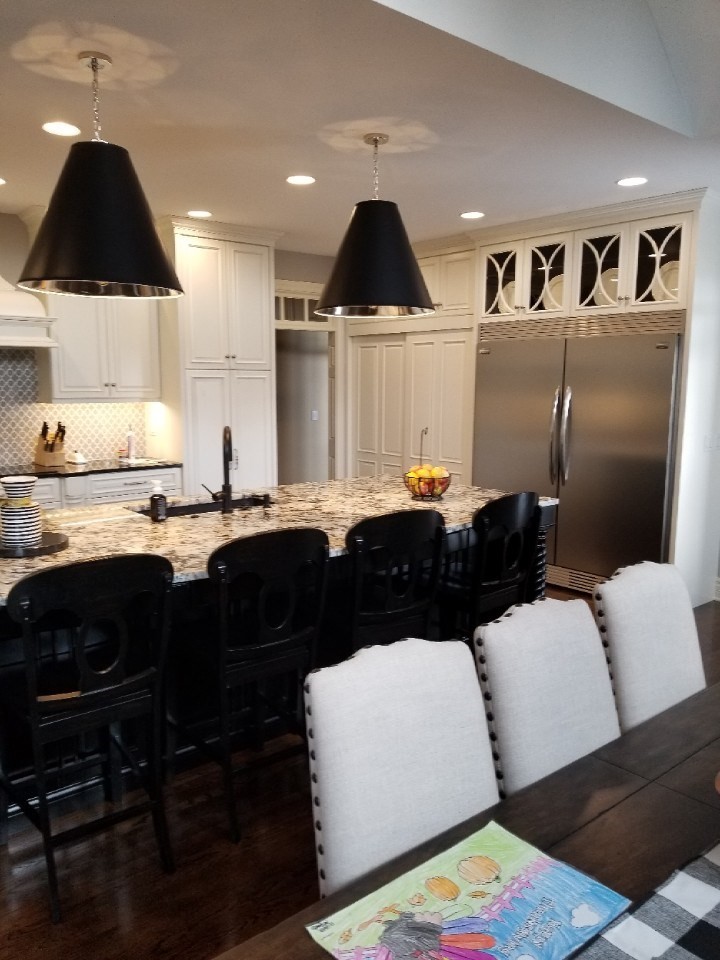 Large transitional single-wall medium tone wood floor and brown floor eat-in kitchen photo with an undermount sink, raised-panel cabinets, white cabinets, granite countertops, gray backsplash, porcelain backsplash, stainless steel appliances, an island and black countertops