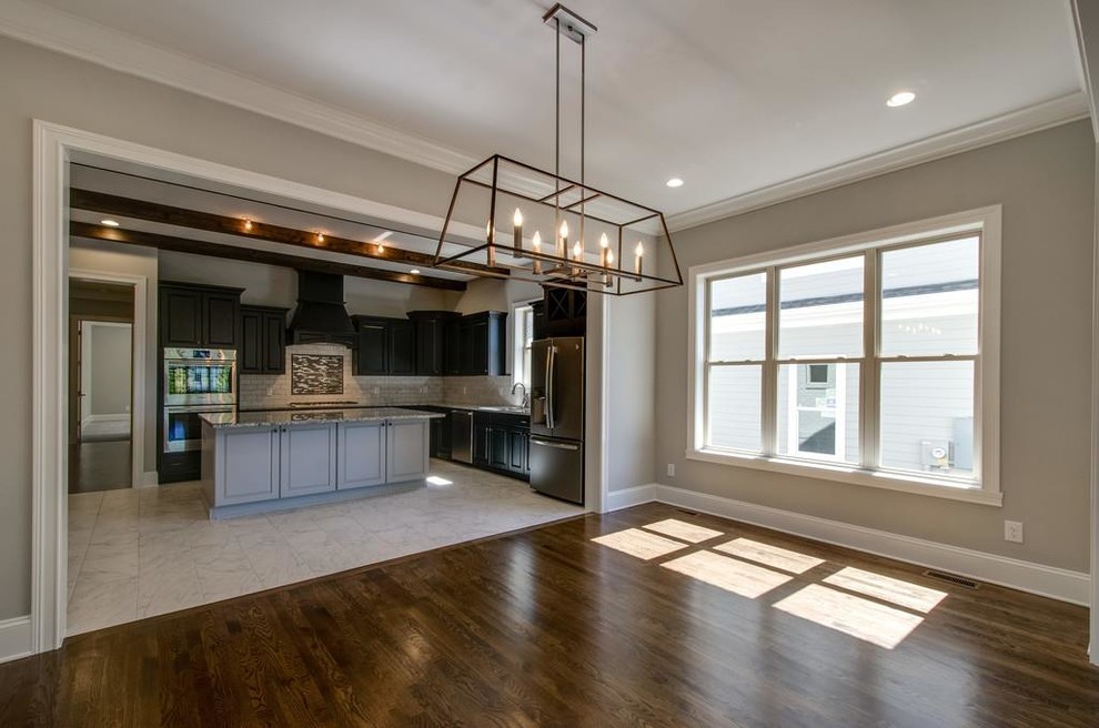 Mid-sized transitional l-shaped ceramic tile and white floor open concept kitchen photo with an undermount sink, raised-panel cabinets, brown cabinets, granite countertops, white backsplash, ceramic backsplash, stainless steel appliances and an island