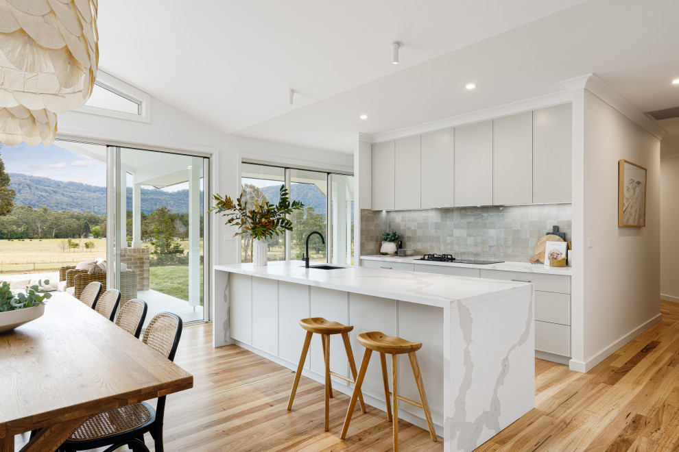 Photo of a medium sized contemporary single-wall open plan kitchen in Wollongong with a submerged sink, all styles of cabinet, grey cabinets, composite countertops, grey splashback, porcelain splashback, black appliances, light hardwood flooring, an island and white worktops.
