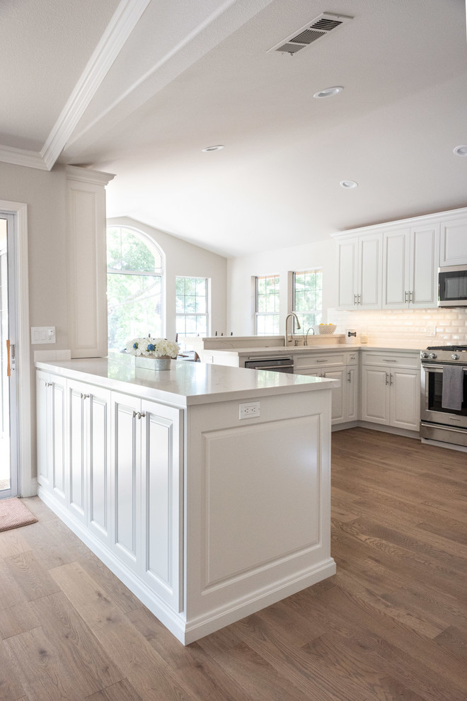 Mid-sized country u-shaped eat-in kitchen in San Luis Obispo with a drop-in sink, raised-panel cabinets, white cabinets, quartz benchtops, white splashback, subway tile splashback, stainless steel appliances, laminate floors, a peninsula, brown floor and yellow benchtop.
