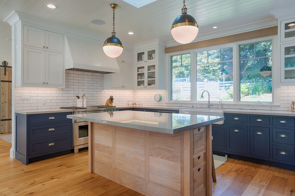 This is an example of a mid-sized country u-shaped eat-in kitchen in San Francisco with a farmhouse sink, recessed-panel cabinets, blue cabinets, quartz benchtops, white splashback, subway tile splashback, coloured appliances, light hardwood floors, with island, beige floor and beige benchtop.