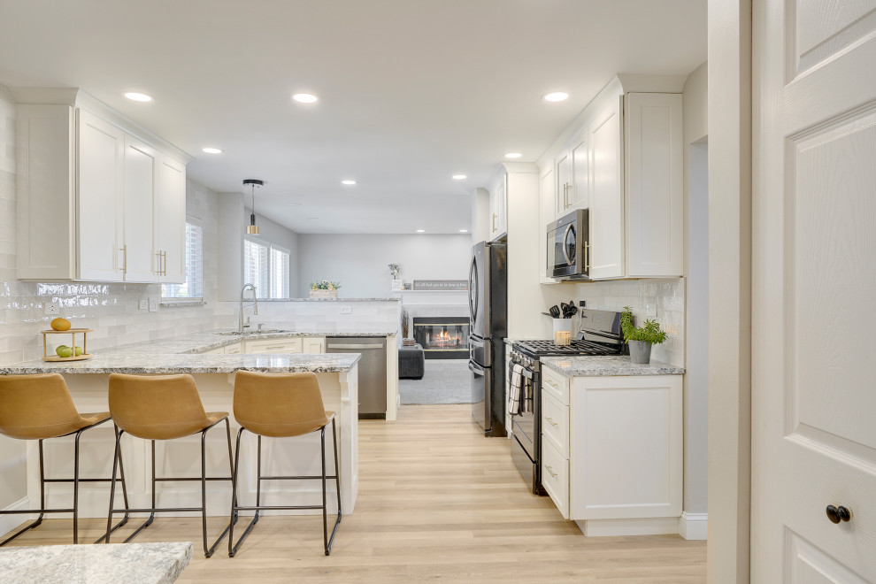 Design ideas for a mid-sized transitional u-shaped open plan kitchen in Chicago with a single-bowl sink, beaded inset cabinets, white cabinets, marble benchtops, white splashback, ceramic splashback, stainless steel appliances, vinyl floors, a peninsula, beige floor and grey benchtop.