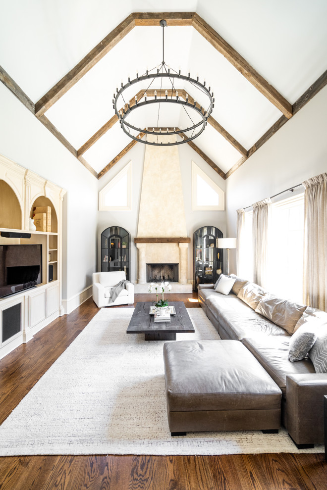 This is an example of a transitional enclosed living room in Atlanta with white walls, medium hardwood floors, a standard fireplace, a built-in media wall, brown floor, exposed beam and vaulted.
